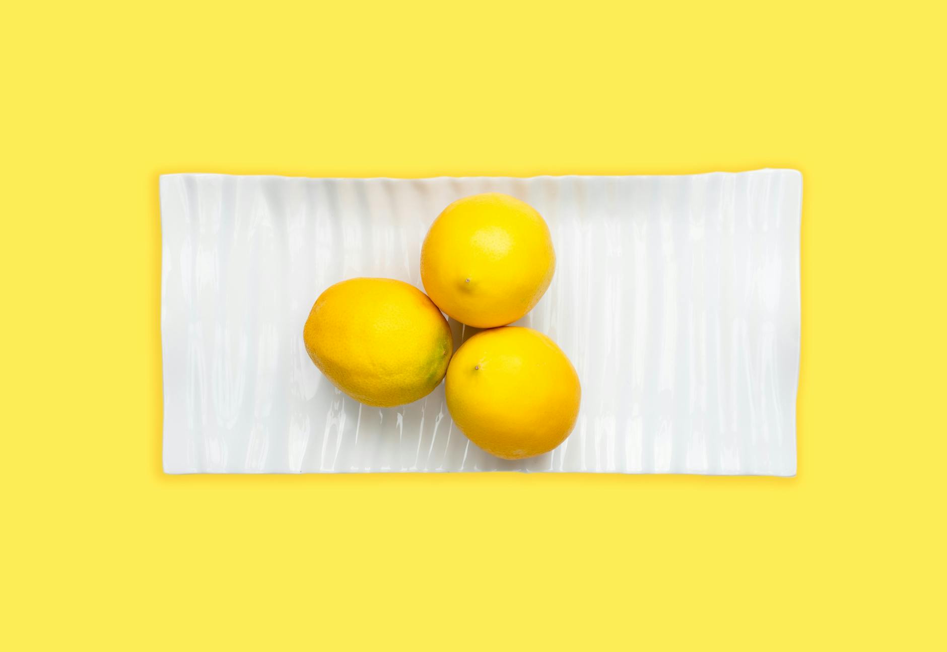 Tre limoni freschi disposti su un piatto bianco con sfondo giallo vibrante