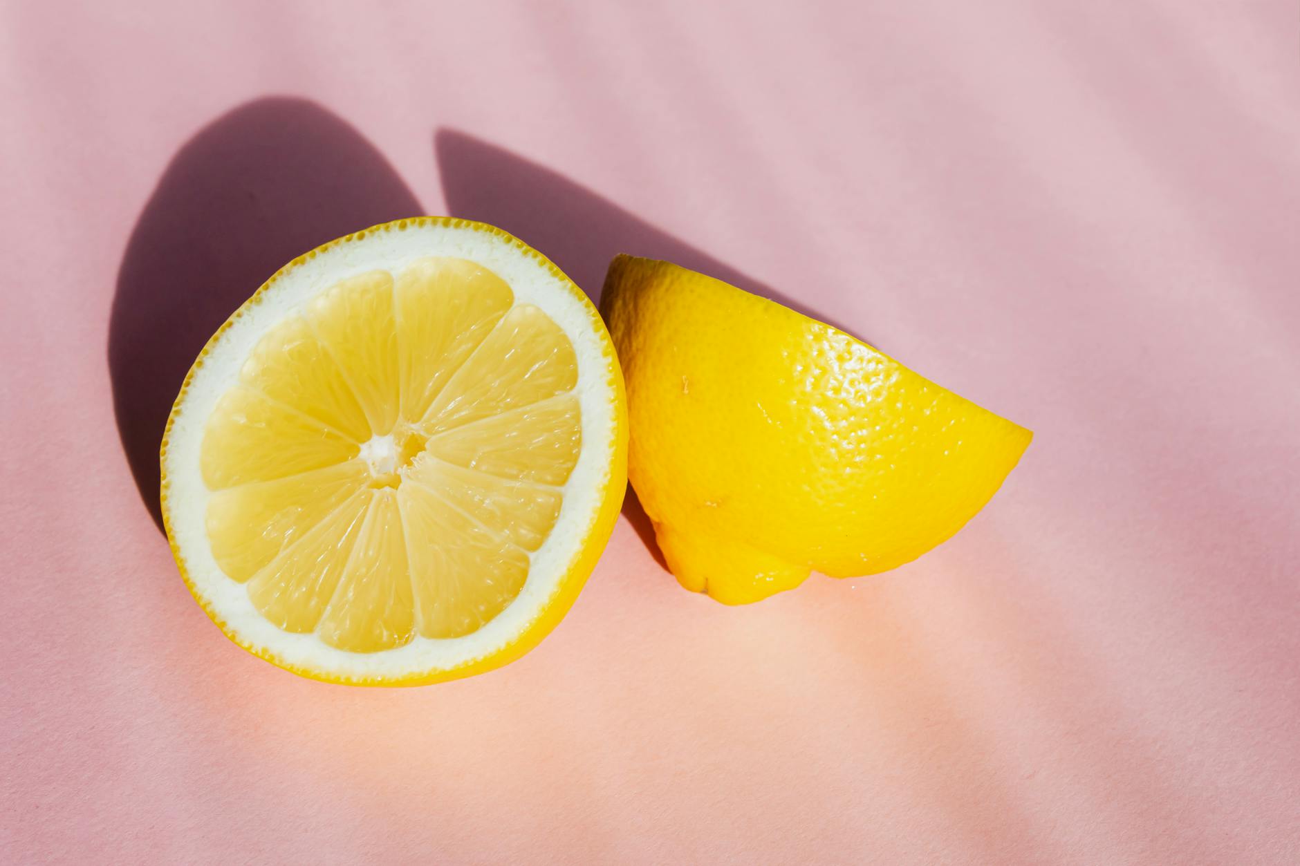 Due metà di limone fresco e succoso su sfondo rosa con raggi di sole