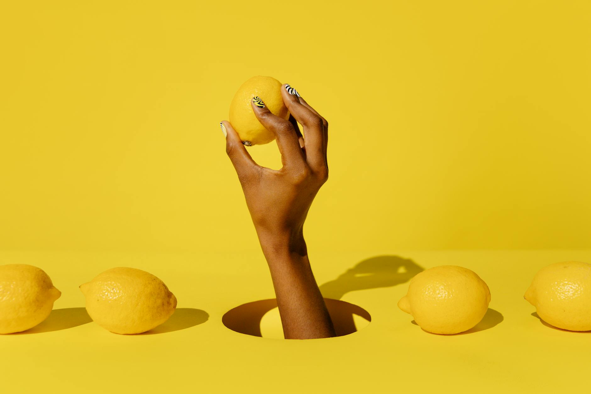 Una mano che tiene un limone fresco su uno sfondo giallo vivido, simbolo di equilibrio e rinascita sessuale