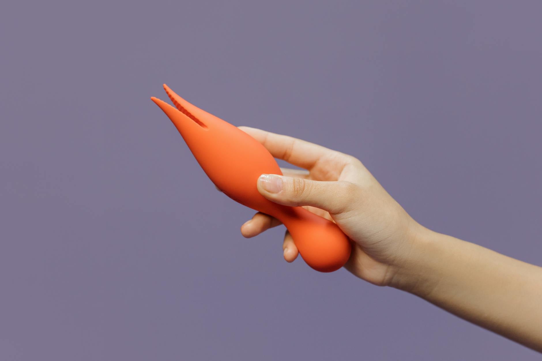 Close-up of a hand holding a modern lemon vibrator against a minimalist purple backdrop
