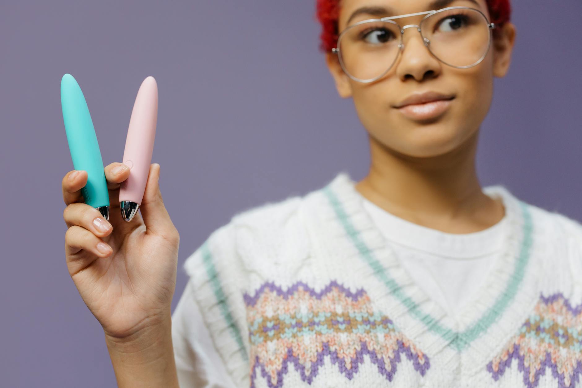Person holding two colorful vibrators against a purple background