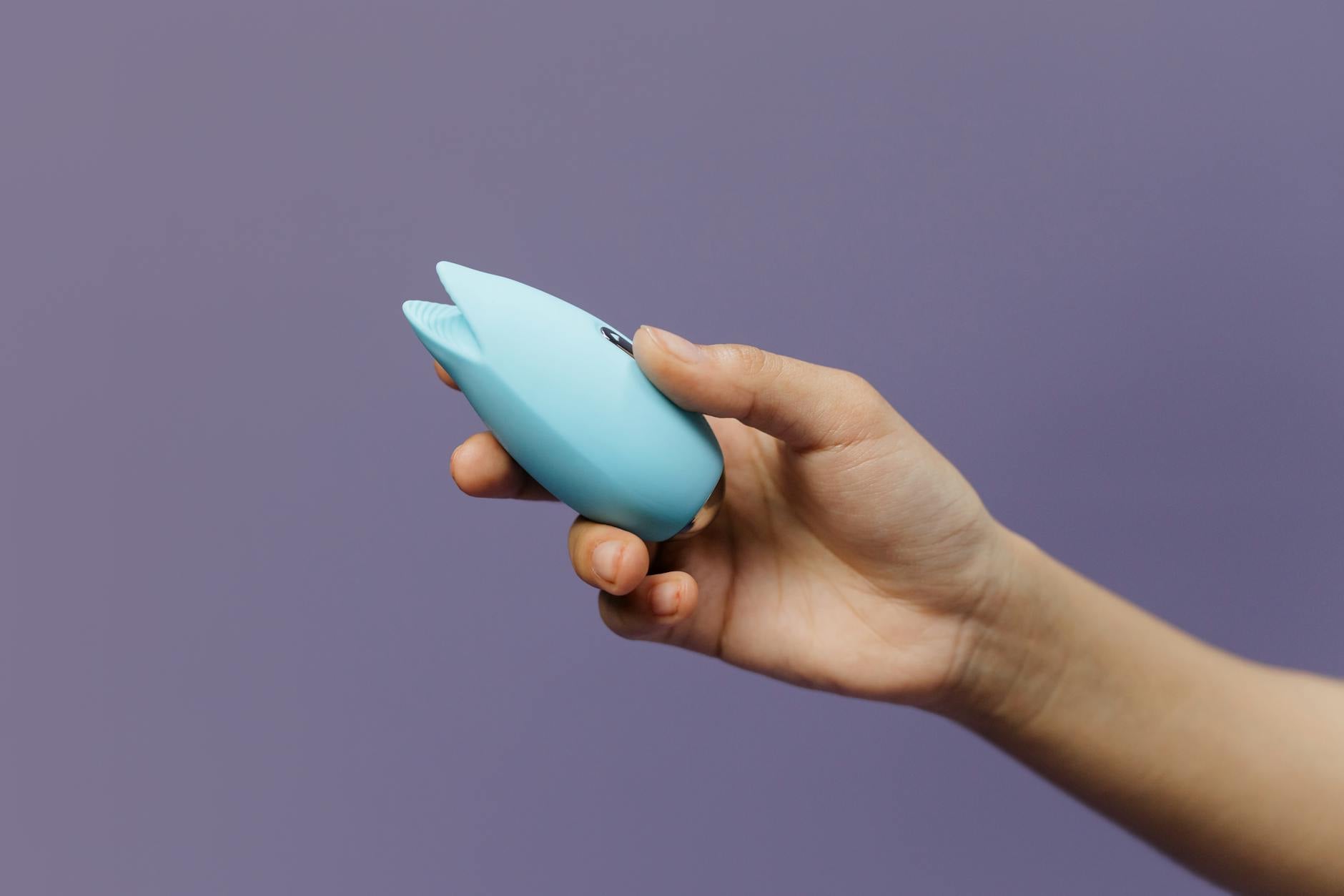 A blue silicone vibrator held in hand against a purple background, symbolizing gentle self-care and postpartum healing