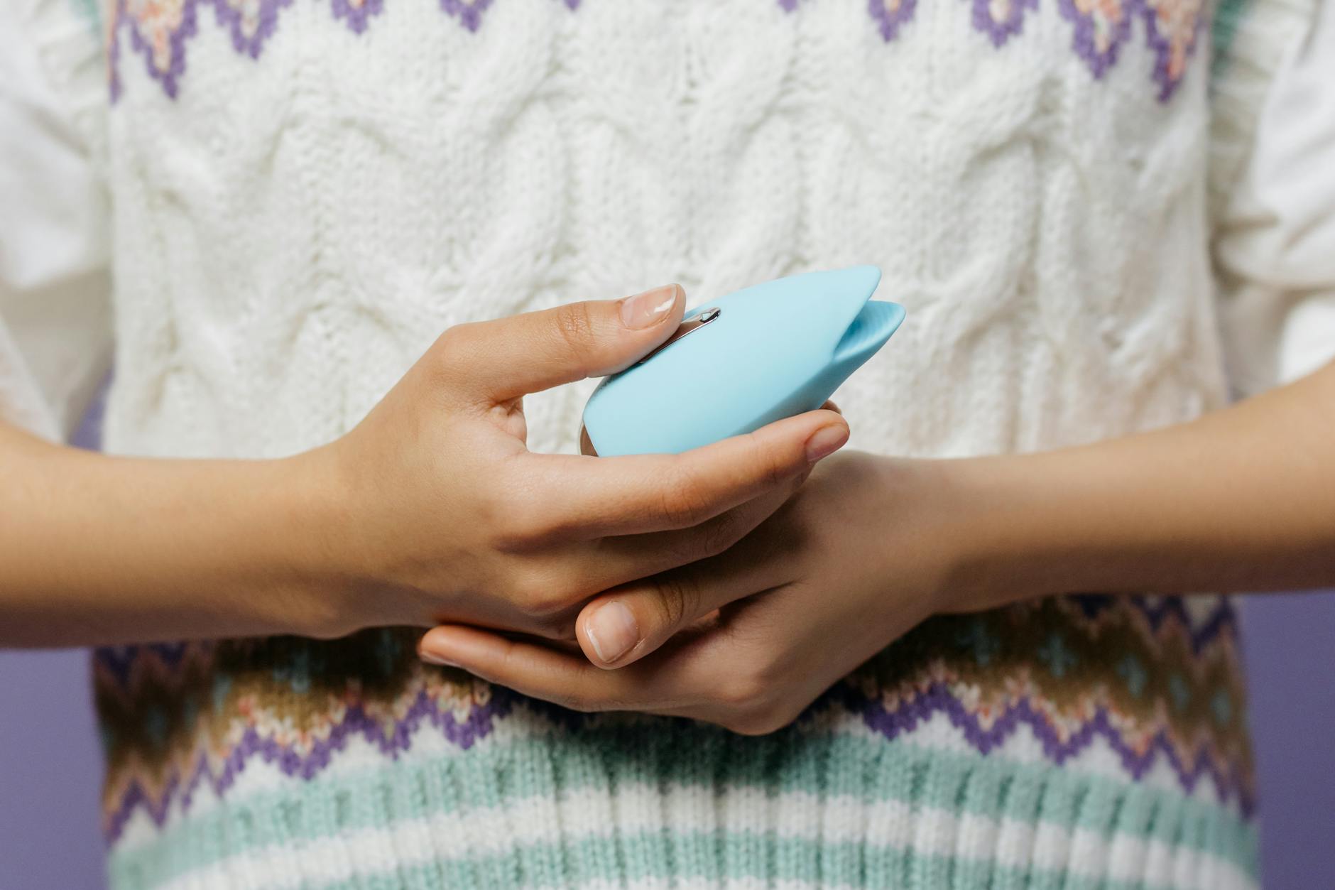 Close-up of hands holding a lemon vibrator against a knitted sweater during an intimate moment.
