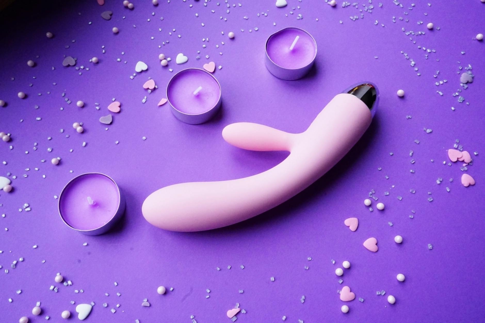 Vibratore rosa su sfondo viola con cuori e candele per un'atmosfera romantica